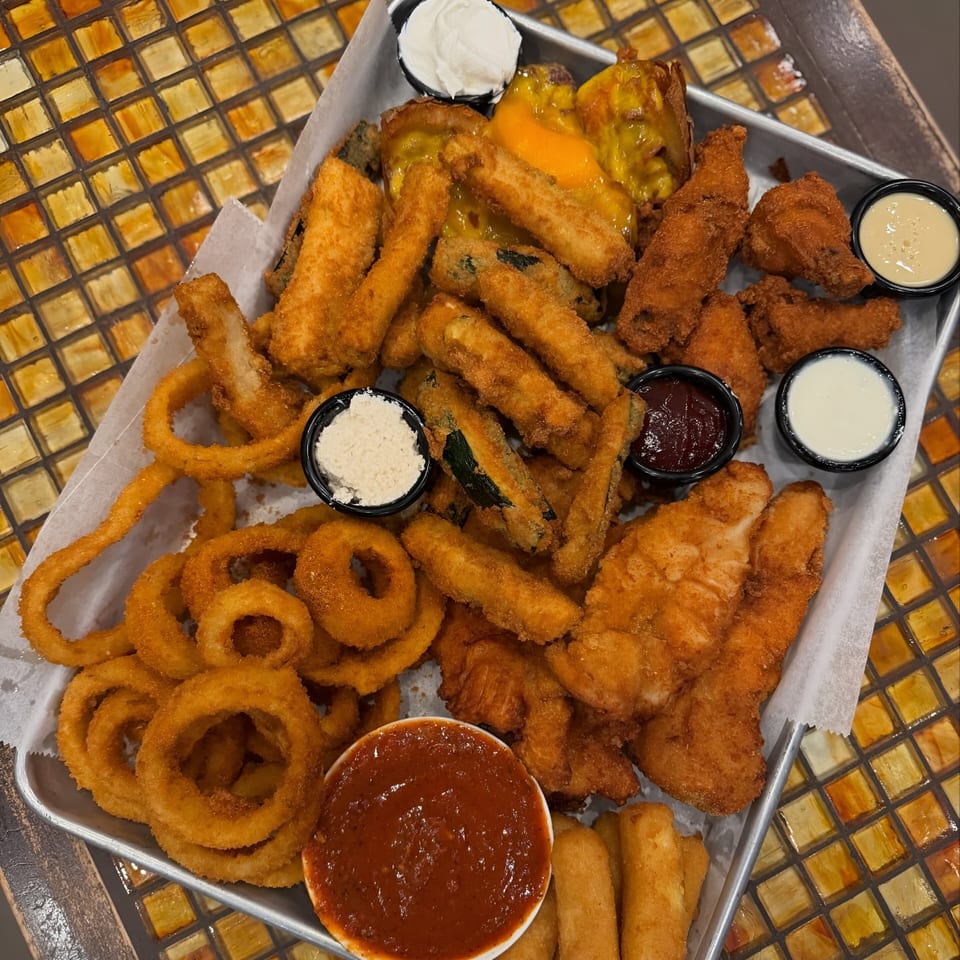 A diner platter of fried onion rings, chicken tenders, mozzarella sticks, and fried zucchini with dipping sauces.