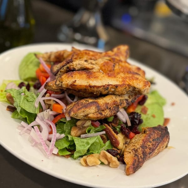 Grilled chicken salad with lettuce, red onions, bell peppers, nuts, and dried cranberries.