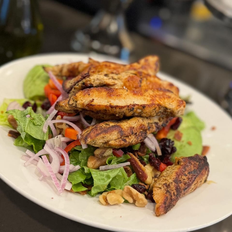 Grilled chicken salad with lettuce, red onions, bell peppers, nuts, and dried cranberries.
